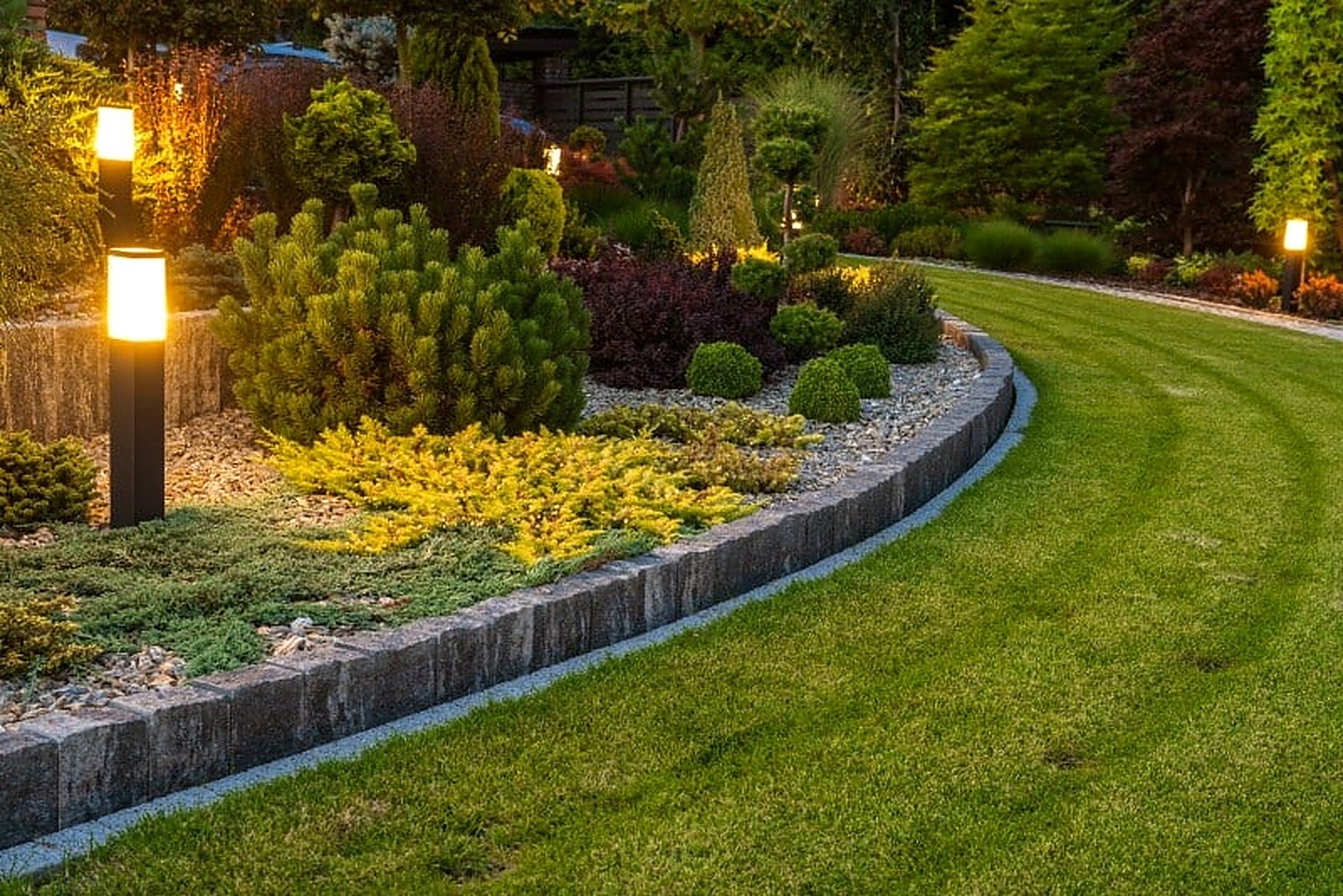 Diseño personalizado de jardín con iluminación y bordes de piedra